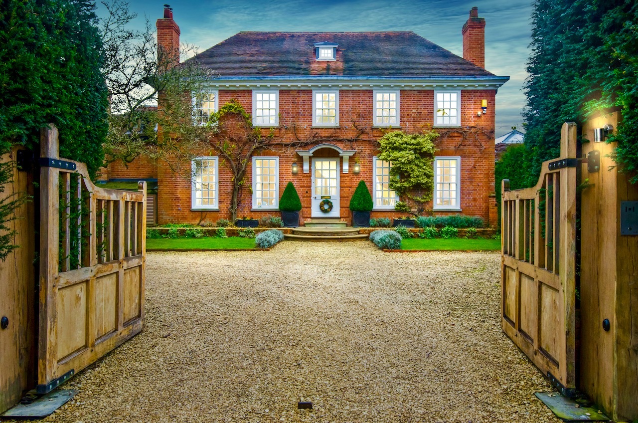 Large brick luxury home with lights shining through large windows